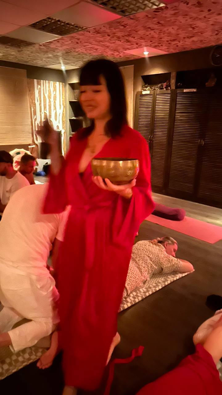 Zarya Tantra holding a singing bowl during a practice gathering; the supplied photograph retains its natural blur.