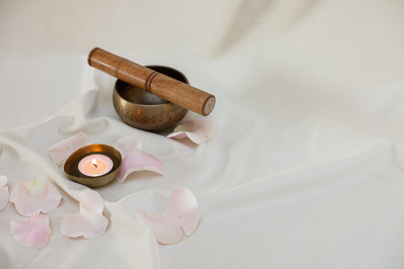 A singing bowl, lit candle and rose petals on white cloth, an illustrative still life for a couples practice.
